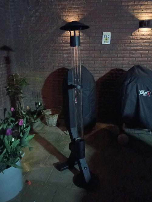Flamesa pellethaard in een schemerige stadstuin naast twee barbecues met beschermhoes