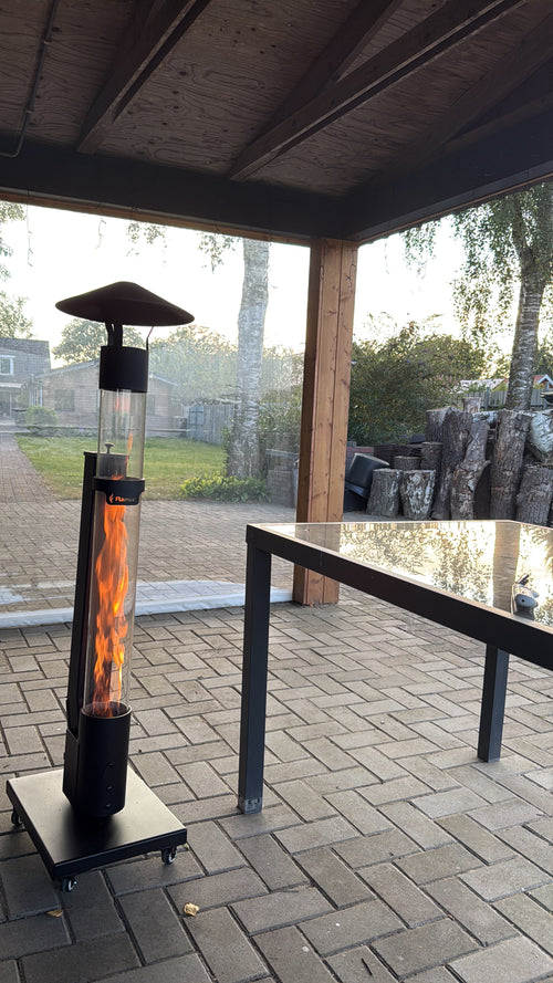 Pelletterrasverwarmer onder een overkapping naast een zwarte tuintafel op een gebakken klinkerterras