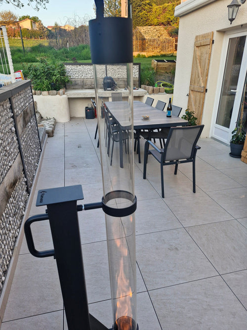 Sfeerhaard voor buiten met glasbuis op de voorgrond en een gedekte tuintafel erachter