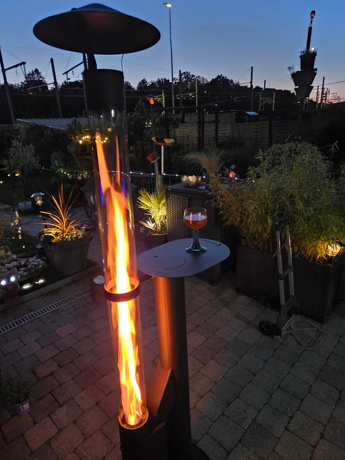 Tuinhaard op pellets met hoge vlam en bijzettafel met een glas cognac in een sfeervolle avondtuin