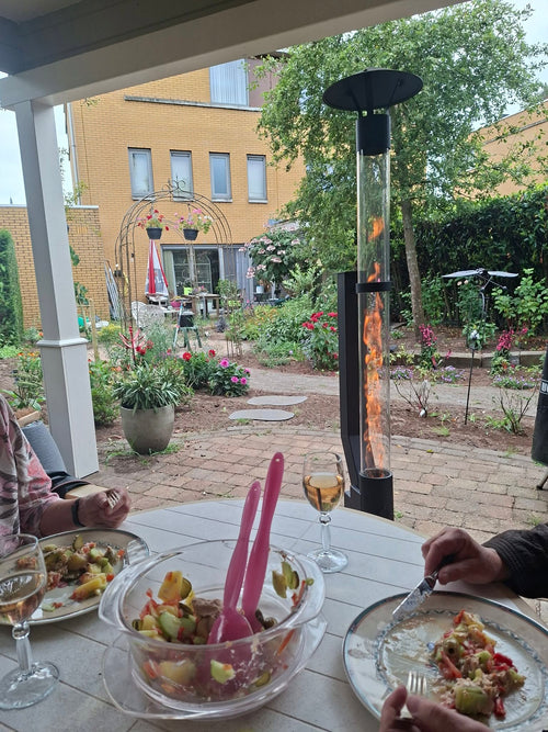 Gezelschap eet buiten aan een gedekte tafel met een brandende tuinhaard op pellets in de tuin