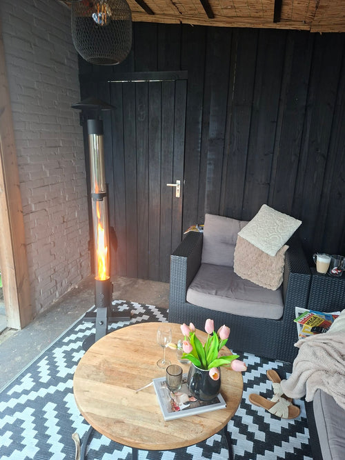 Terraskachel op pellets in een donkere tuinkamer met een rieten fauteuil en ronde houten tafel