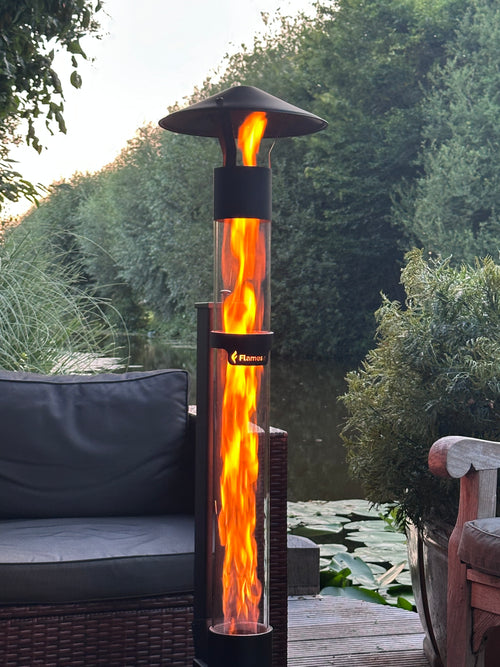 Close-up van de vlammenzuil van een Flamesa pellethaard met vijver en groen op de achtergrond