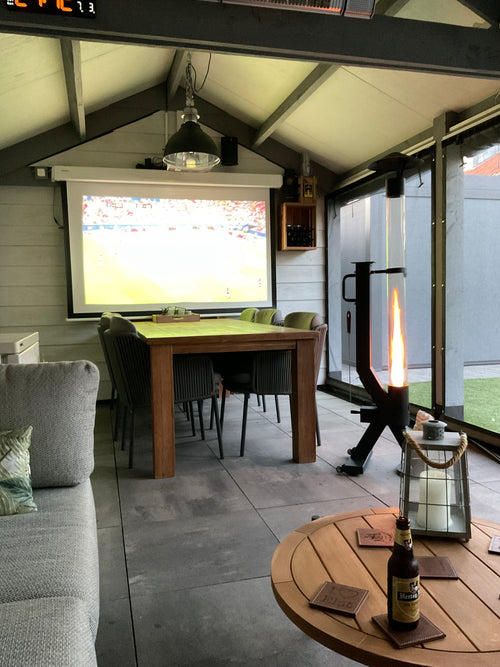 Buitenhaard op pellets in een tuinhuis met projectiescherm, loungebank en houten salontafel