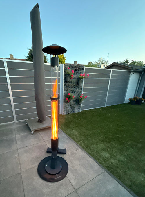 Terraskachel op pellets brandt naast een ingeklapte parasol in een tuin met kunstgras en schutting