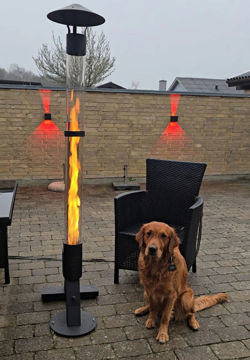 Golden retriever zit naast een brandende pelletterrasverwarmer op een terras met infraroodstralers