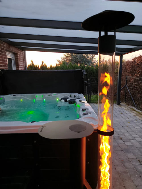 Sfeerhaard voor buiten brandt met tafelblad naast een groen verlichte jacuzzi op een terras