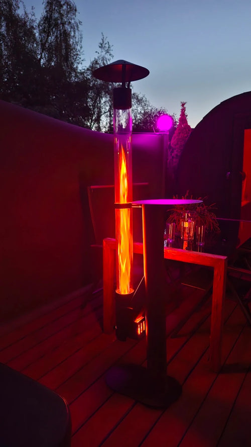 Vuurzuil op pellets op een vlonder met roze sfeerverlichting en een bijzettafel bij avond