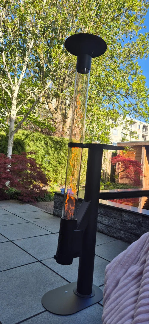 Terrasverwarmer op pellets brandt op een terras met bijzettafel en een bloeiende tuin op de achtergrond