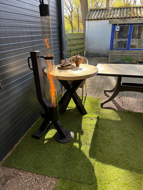 Flamesa pelletkachel brandt bij een ronde houten tafel op kunstgras langs een zwarte gevel