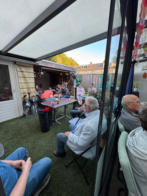 Familie zit op klapstoelen in de tuin bij een Flamesa pelletkachel onder een veranda
