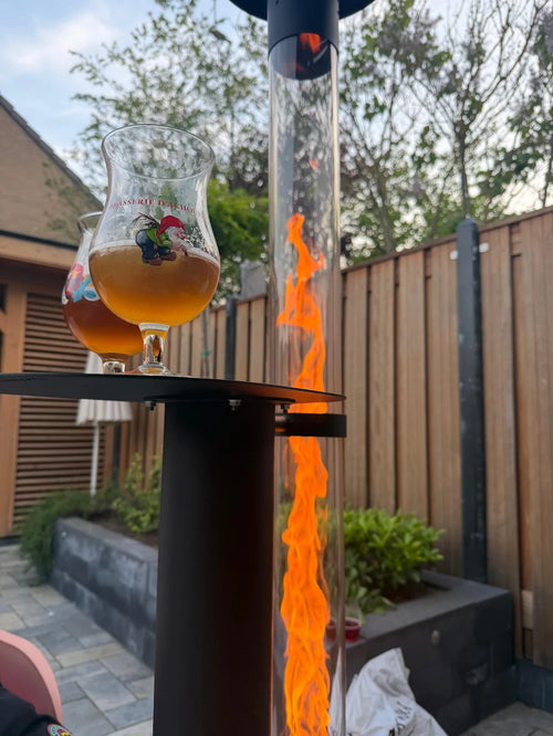 Glas bier op het tafelblad van een brandende pelletterrasverwarmer in een stadstuin