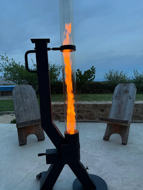 Flamesa pelletkachel voor buiten met hoge vlam tussen houten stoelen op een terras bij schemer