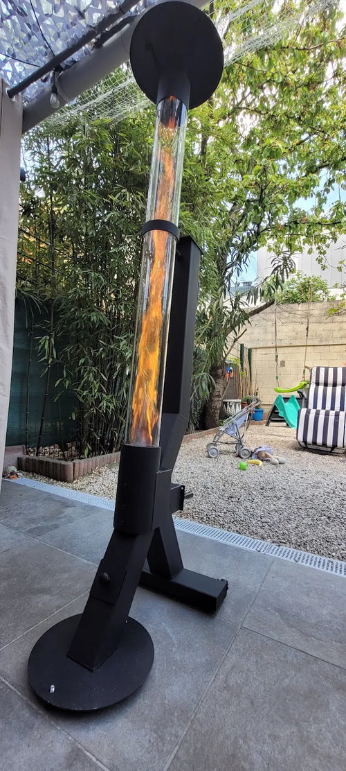 Tuinhaard op pellets met ronde voet brandt op een terras met strandstoel en groene schutting