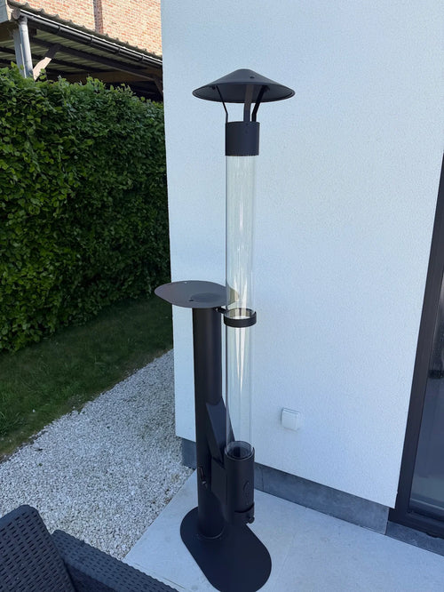 Flamesa terraskachel op pellets met glasbuis en bijzettafel tegen een witte muur op grind