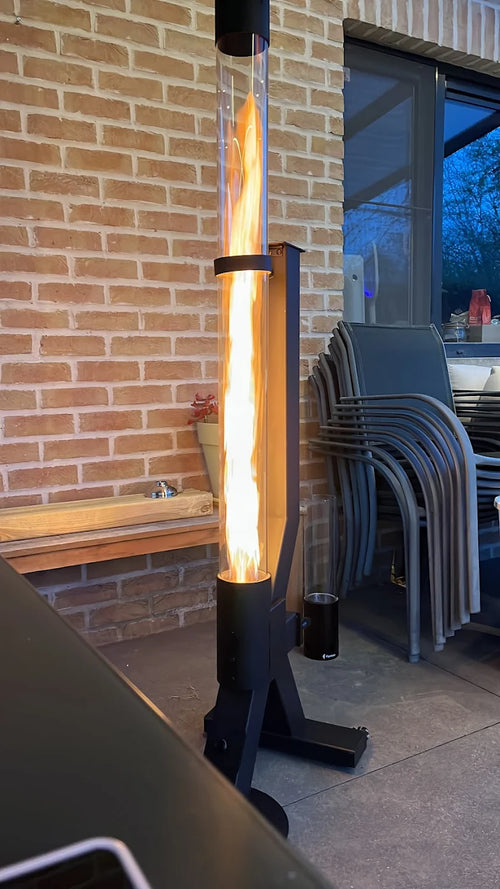 Terrasverwarmer op pellets brandt tegen een bakstenen muur naast een stapel tuinstoelen
